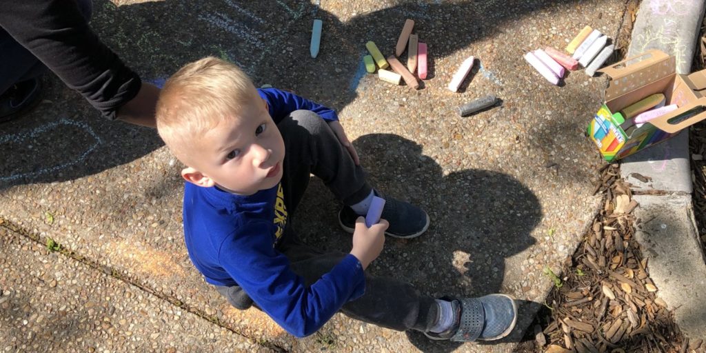boy outside coloring with chalk, looking up at camera