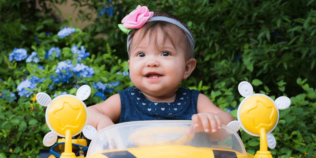 Infant with headband in a car with bumblebees in the foreground with flowers in the background.